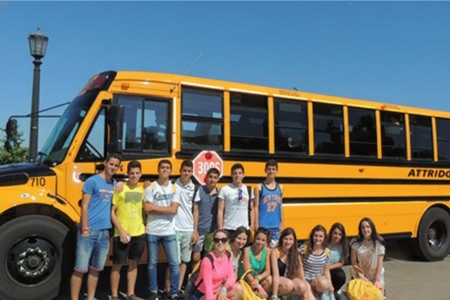 Grupo de estudiantes frente a autobús escolar amarillo antes de iniciar cursos en el extranjero y preparación académica de idiomas.